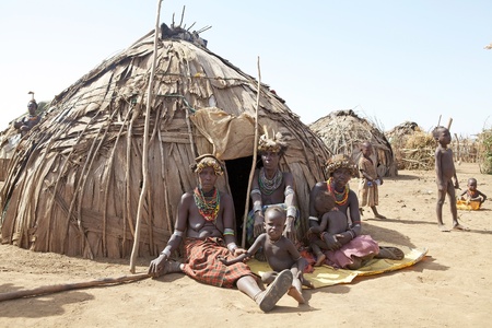 Omorate, Ethiopia, February 17, 2013: african women of the Dasanch or Galeb ethnic group with tribal clothes, hairstyle and necklaces are sitting, with children, outside the hut at the village near Omorate.のeditorial素材