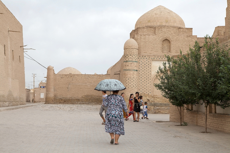 Uzbeck woman with umbrella is walking along the street at Itchan Kala, Khiva, Uzbekistan. Itchan Kala is the walled inner town of the city of Khiva. Since 1990 it has been protected as a World Heritage Site. The old town retains more than 50 historic monuのeditorial素材