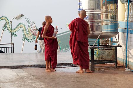 Buddhist monks with traditional robes are filling in the bottles of water at the tank at the Kyaiktiyo Pagoda, Golden Rock, Kyaiktiyo, Myanmar or Burma. Kyaiktiyo Pagoda also known as Golden Rock is a well known Buddhist pilgrimage site in the Mon State, のeditorial素材
