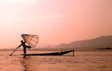 Leg fishing on the Inle Lake at the sunset Myanmar or Burma. Burmese fisherman on boat is catching fishes by traditional netの写真素材