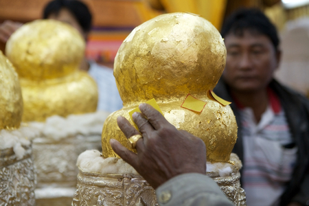 Pilgrim is putting a gold leaf on the Buddha image at the Phaung Daw Oo Pagoda, Lake Inle, Myanmar. Phaung Daw Oo Pagoda is a noteble buddhist site in Myanmar or Burma. The pagoda houses five small gilded images of Buddha, wich have been covered in gold lのeditorial素材