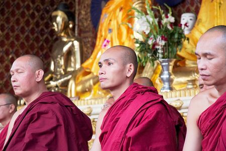 Buddhist monks in traditional robes in meditation at the Shwedagon Pagoda, a gilded stupa located in...