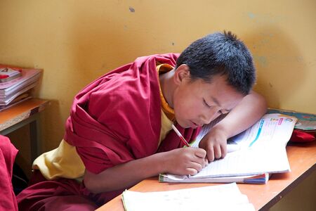 Sikkimese Buddhist child in traditional robes is attending a lesson in the classromm at the Labrang...