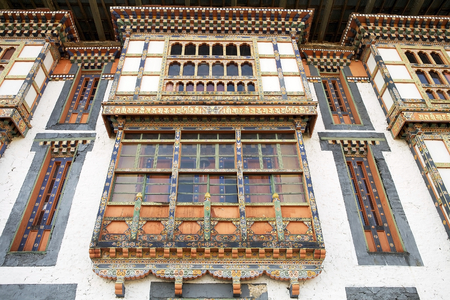 Wooden frontage with small arched windows at the Kurjey Lhakhang also known as Kurjey Monastery, located in the Bumthang Valley in the Bumthang District, Bhutan. This is the final resting place of the first three King of Bhutan. Also, a large tree behind の写真素材