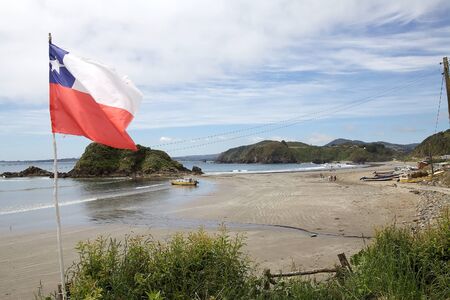 View of Punihuil beach with flag of Chile in the northwestern cost of Greater Island of Chiloe, Chile. Punihuil is a cove with a small community. Three small island lie to the west and north of the cove and they are a breeding site for Humboldt and Magellのeditorial素材