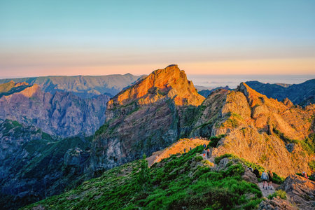 Madeira - A sunset view from a mountain peak with hikers on a scenic trail, surrounded by rugged rocky terrain.の写真素材