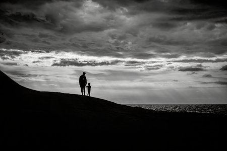 Xwejni Salt Pans, Malta - A silhouette of a father and child holding hands against a cloudy sky with the ocean in the background.の写真素材