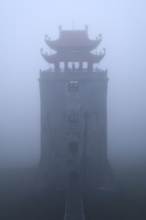 A mystical, foggy view of a traditional pagoda on Mount Fansipan, Vietnam. The dense mist adds an ethereal, haunting ambiance to the ancient structureの写真素材
