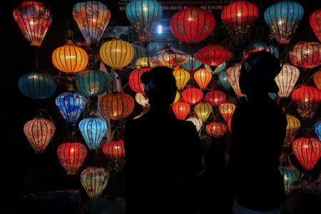 Silhouettes of two people admire a vibrant display of colorful lanterns at night in Hoi An, Vietnam, creating a stunning visual contrast.の写真素材