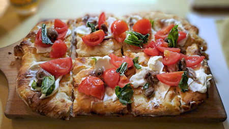 Freshly baked pizza with cherry tomatoes, mozzarella, olives, anchovies, and basil on a wooden board.の写真素材