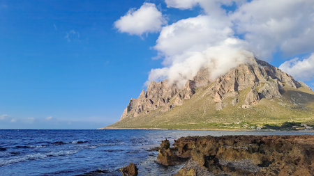 Rocky mountain near Custonaci in Trapani province, Sicily, partially covered by clouds, with sea in the foreground.の写真素材