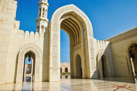 Ornate stone arches and minaret of a mosque under clear blue sky. Islamic architecture with detailed carvings and marble flooring.の写真素材