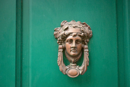 Vintage bronze door knocker shaped like a woman's head with classical features, mounted on a green wooden door.の写真素材