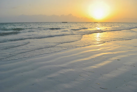 Sunset over calm ocean waves with wet sand reflecting golden light on a tranquil beach.の写真素材