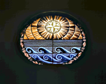 Stained glass window featuring a stylized sun above ocean waves, with geometric and symbolic patterns, glowing in warm and cool tones.の写真素材