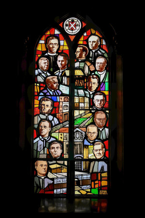 Colorful stained glass window depicting portraits of priests and historical figures, surrounded by architectural and symbolic elements in a dark interior of a church.の写真素材