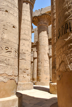 Massive stone columns covered in ancient Egyptian hieroglyphs inside the Karnak Temple, lit by strong sunlight with deep shadows creating dramatic contrast.の写真素材