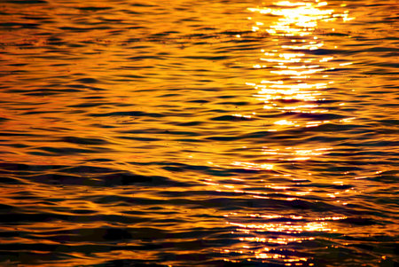 Close-up of golden sea surface with shimmering reflections of the setting sun.の写真素材
