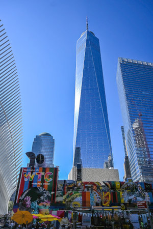 Modern glass skyscrapers including One World Trade Center in New York City, with colorful murals and street vendors in the foreground under a clear blue sky.の写真素材