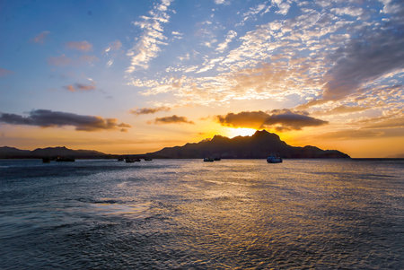 Sunset over the sea with fishing boats and dramatic clouds, mountains silhouetted on the horizon.の写真素材