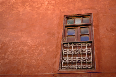 Old wooden window with metal bars on a red stucco wall. Architectural detail from a traditional building.の写真素材
