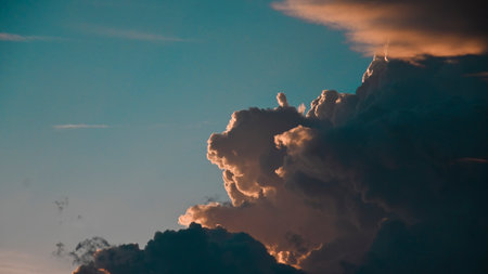 Close-up view of dramatic cumulonimbus clouds illuminated by sunlight at sunset, set against a clear sky.の写真素材