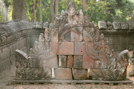 Ancient sandstone temple carving with intricate details standing in forest ruins, part of historic Southeast Asian architecture.の写真素材
