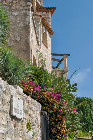 Stone house with flowering plants, cactus, and a sign "La BohÃ©mienne" on a sunny day in a Mediterranean-style gardenの写真素材