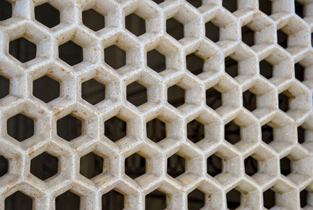 Close-up of a stone lattice with hexagonal openings, forming a honeycomb pattern in beige color.