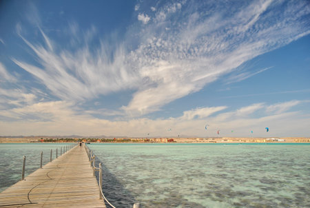 Long wooden pier leading to the shore of a turquoise sea with kite surfers and resort buildings in the background, Egyptの写真素材