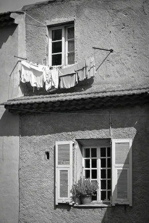 Old stucco house with wooden shutters, a flower pot in the window, and laundry drying on a line, black and white street sceneの写真素材