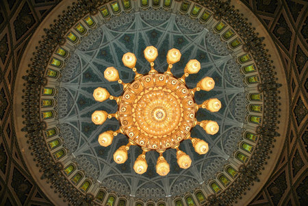 Looking up at a large ornate chandelier centered in a richly decorated mosque dome. Symmetrical Islamic architecture with stained glass windows.の写真素材