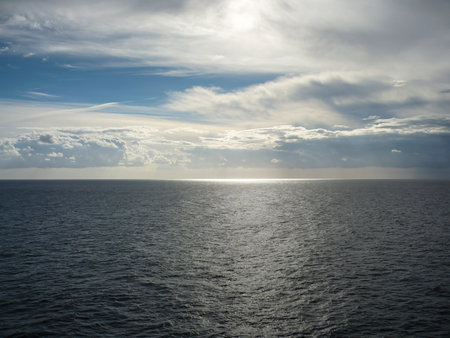 Vast open sea under dramatic clouds with sunlight breaking through, creating a silver reflection on the ocean surfaceの写真素材