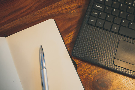 Blank notepad, silver metal pen and black laptop on top of a solid oak surface.