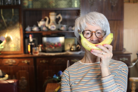 Cheerful senior woman covering mouth with a banana