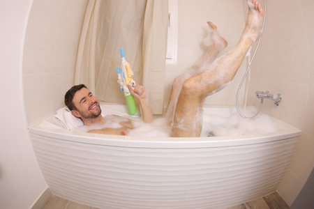 Adult man using water gun in the bathtub&nbsp;の写真素材