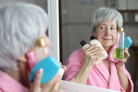 Senior woman holding a bunch of skin care cosmetics in the bathroomの写真素材