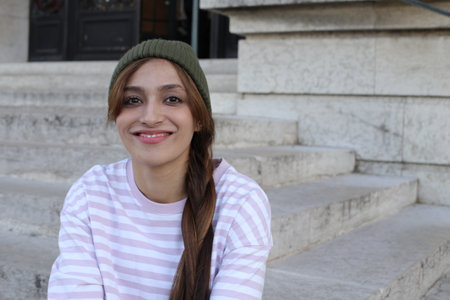 A young fashionable woman in her twenties is wearing a green beanie ,and a pink and white striped...