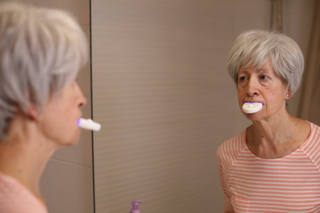 Senior woman whitening her teeth at home