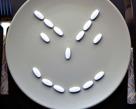 Concept of drug push by pharmaceutical companies and drug addiction. Plate full of tablets, cunning smile with knife and fork, plate of medicine, plate of drugsの写真素材