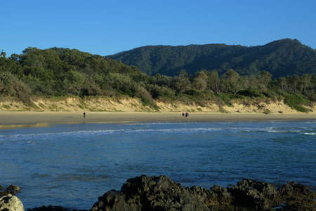View of a beach, sand, rock, sea waves, hills, mountain, trees and a unidentifiable surfer in sea New South Wales Australiaの写真素材