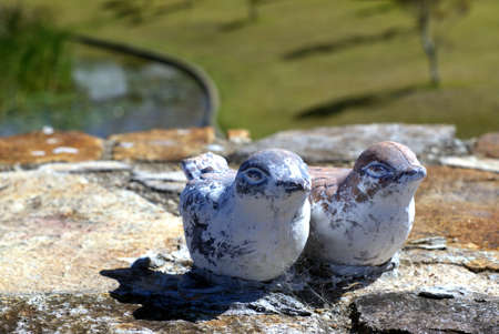 Garden statues of two ducks. Worn off terracotta garden ornaments of birds sitting on stone wall.の写真素材