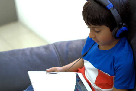 Kid using technology shot in natural light. Kid wearing headphones looking at tablet computer. Child with headphones using tablet.の写真素材