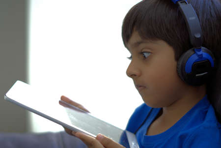 Kid using technology shot in natural light. Kid wearing headphones looking at tablet computer with...