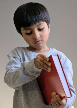 Kid checking book out. Boy holding a book, trying to open book. Kid looking into the book, not at the camera. Shot in natural light only.の写真素材