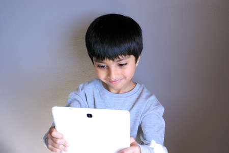 Kid looking at tablet screen taking selfie. Selective focus, natural light. Kid smiling looking towards tablet computer. Child using technology. Happy kid using tablet.の写真素材