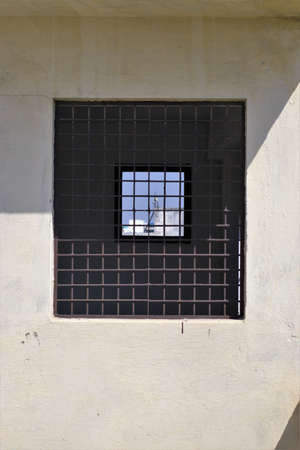 Small window inside big window. Grilled window in wall. Wall is partly under sunlight and partly...