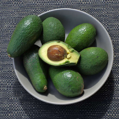 Green avocados in bowl with one half cut ripe avocado and seed. Shot from the top in natural light...