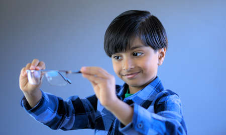 Smiling kid checking eye glasses before wearing them. Child in act of wearing glasses. Subject...
