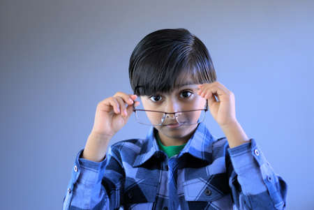 Smart kid putting eye glasses on. Child in act of wearing glasses. Subject looking at lens.の写真素材